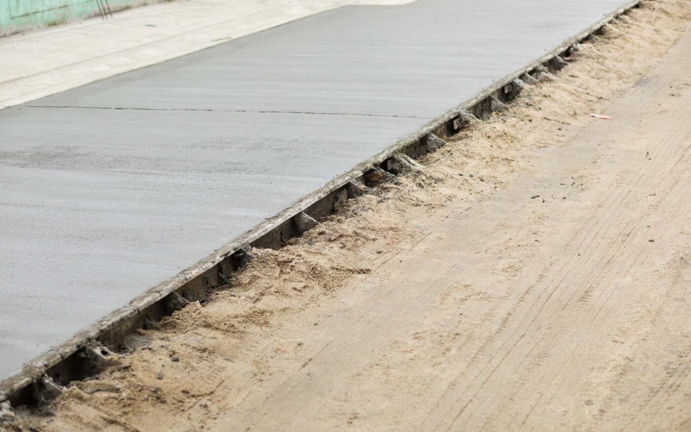 A close-up of a freshly paved smooth concrete road segment under construction in West Palm Beach, FL. The right side shows a trench filled with compacted soil, awaiting paving by the restoration contractor. The sidewalk and surrounding area are partially visible.